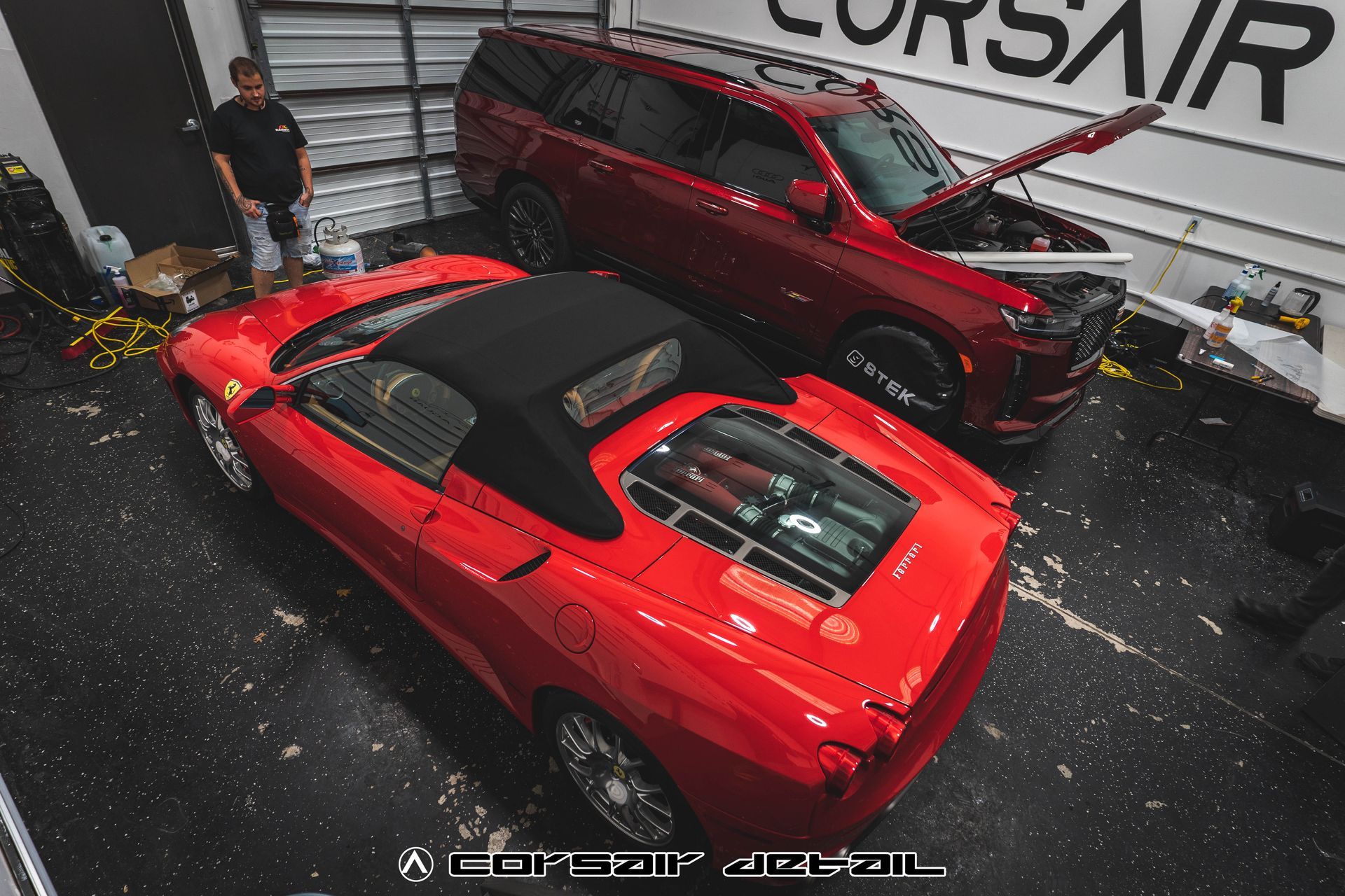 A red car is parked next to a red suv in a garage.