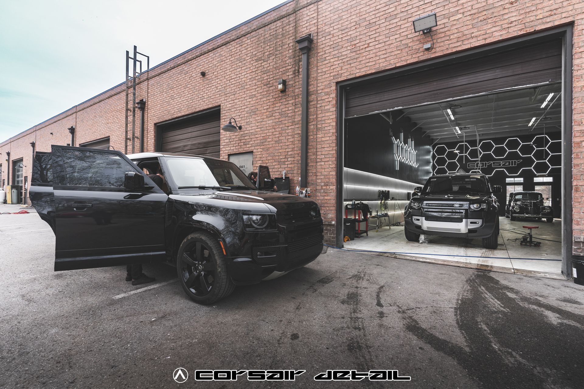 A black car is parked in front of a brick building.