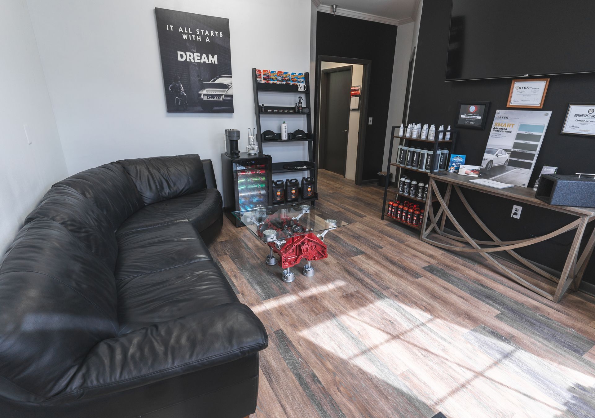 A office with a black leather couch and a wooden floor.