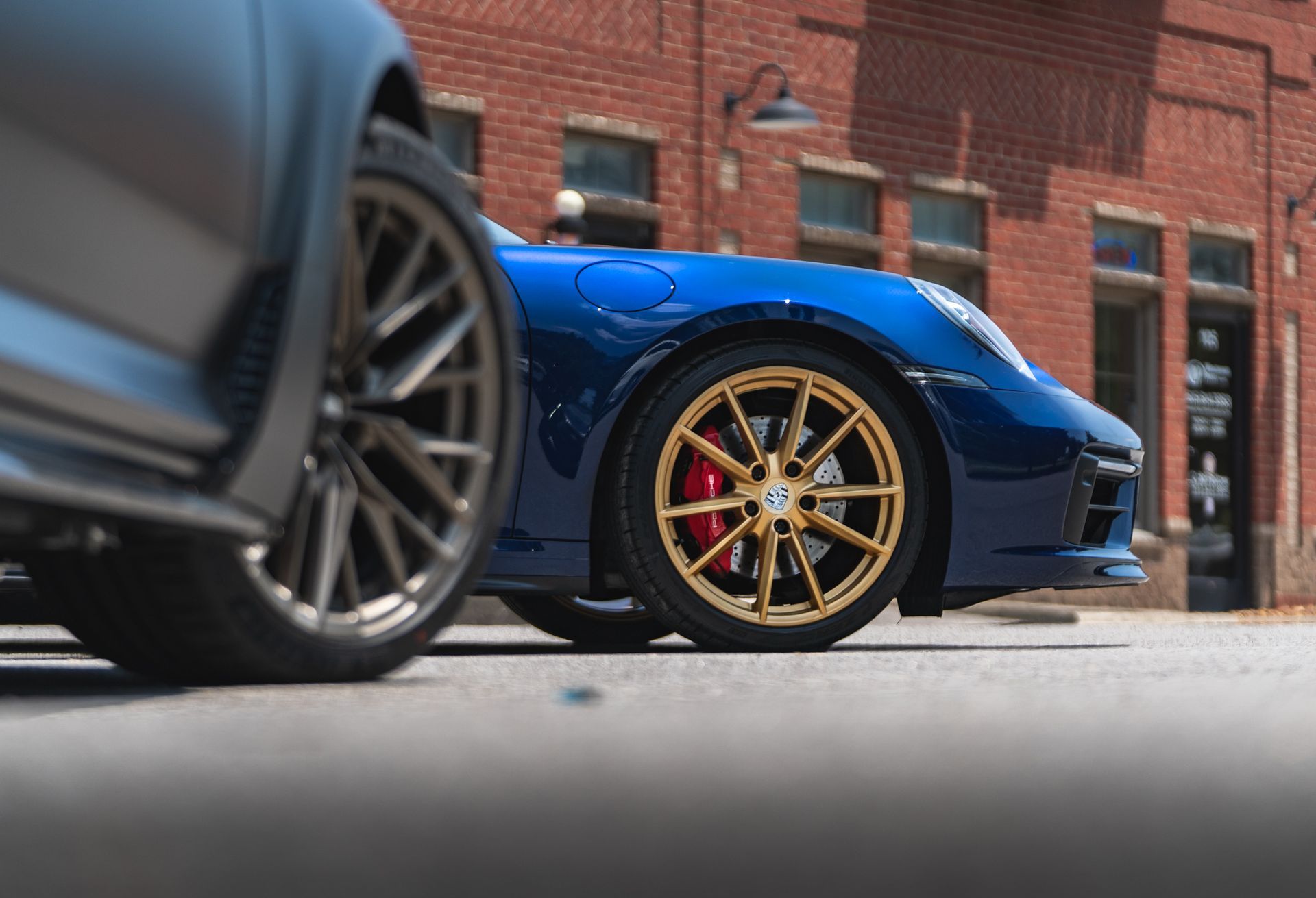 Two sports cars are parked on the side of the road in front of a brick building.