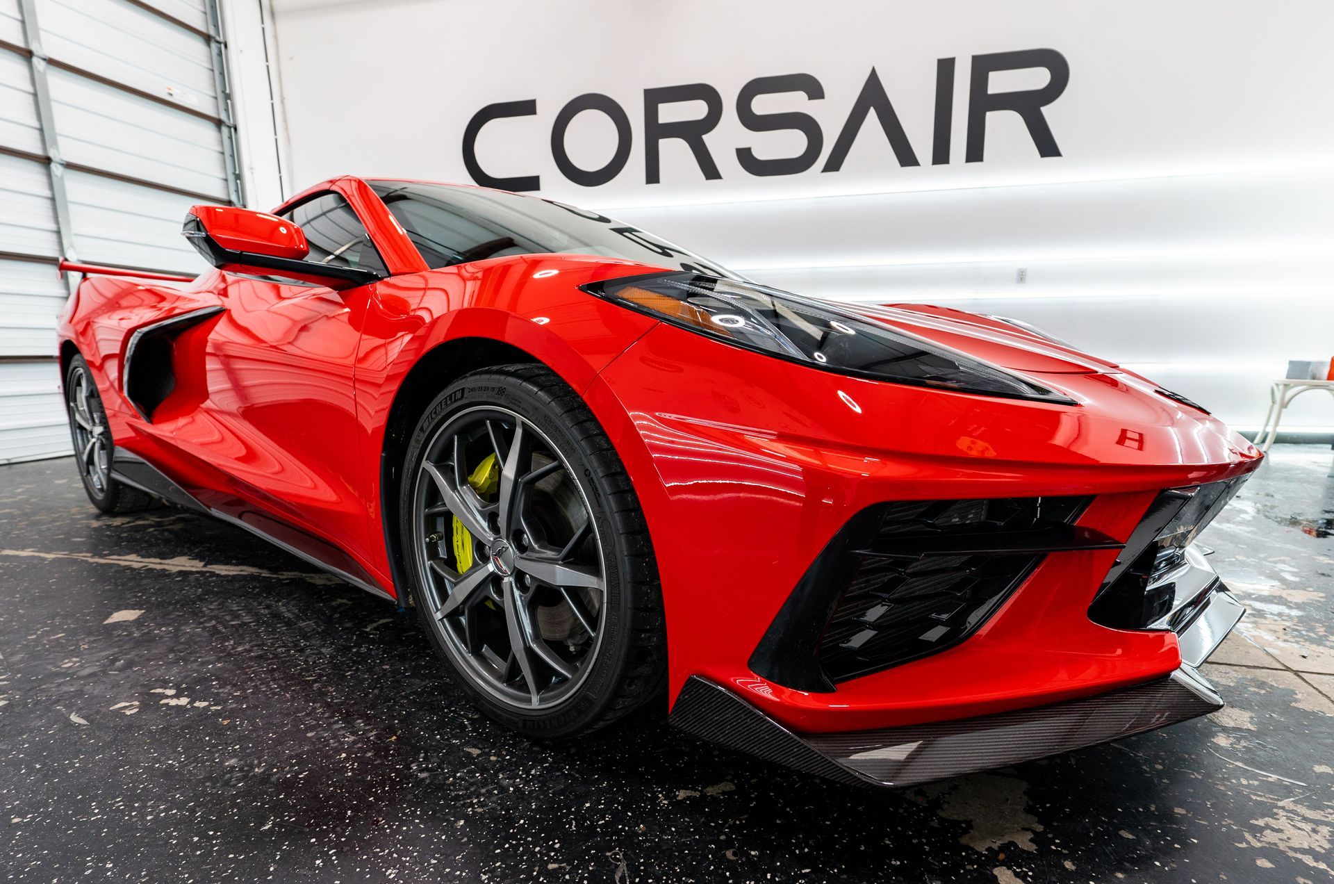 A red sports car is parked in front of a sign that says corsair.