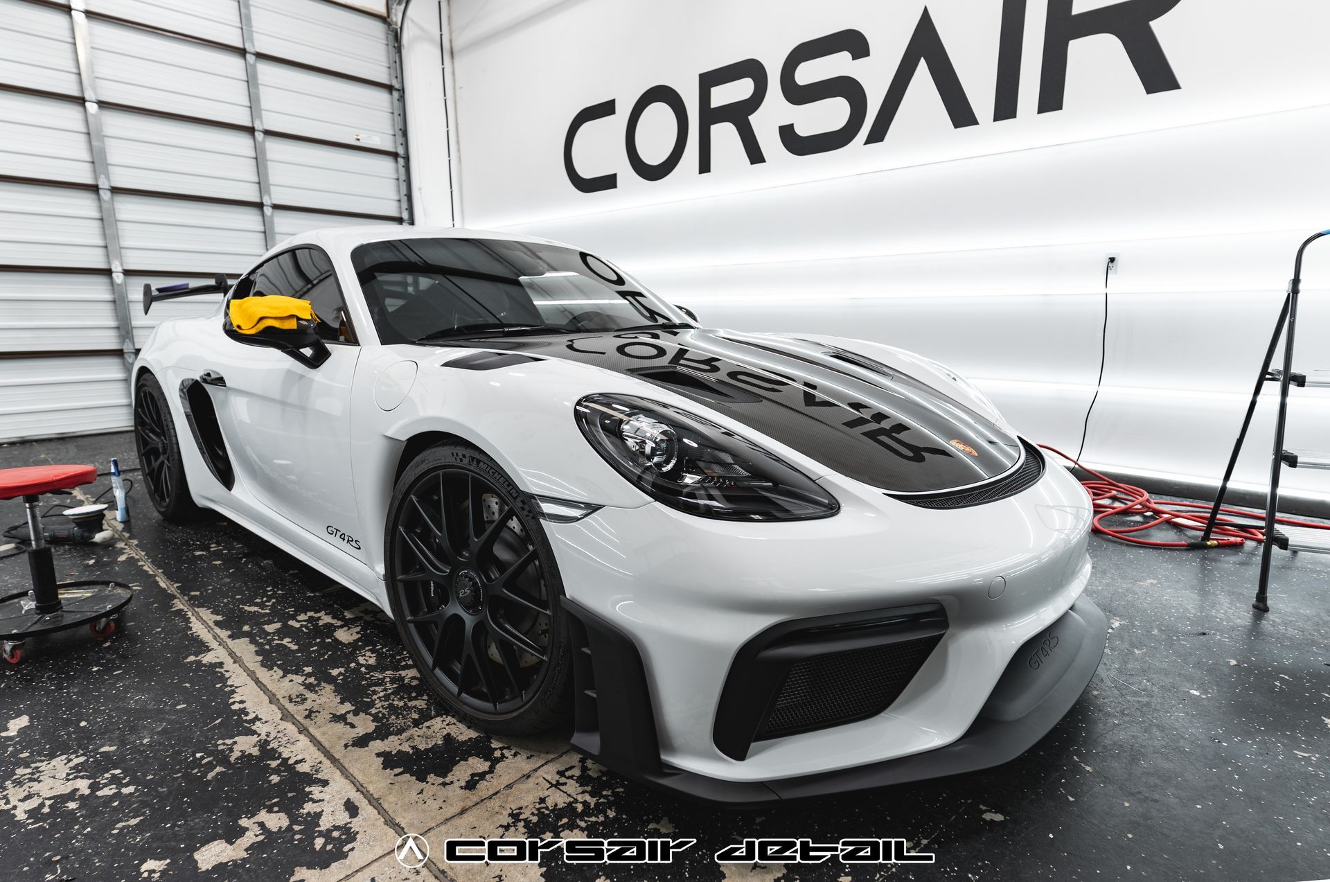 A white sports car is parked in a garage next to a sign that says corsair.