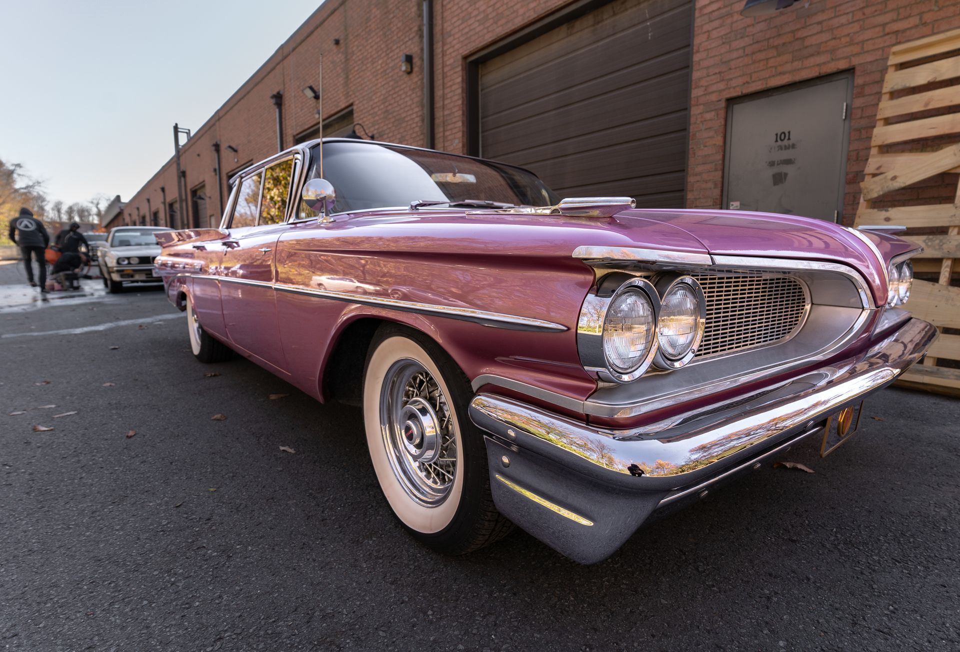 A pink car is parked in front of a brick building.