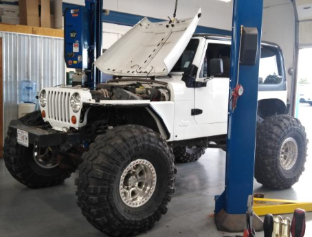 A white jeep with the hood up is on a lift | A2Z AutosLLC