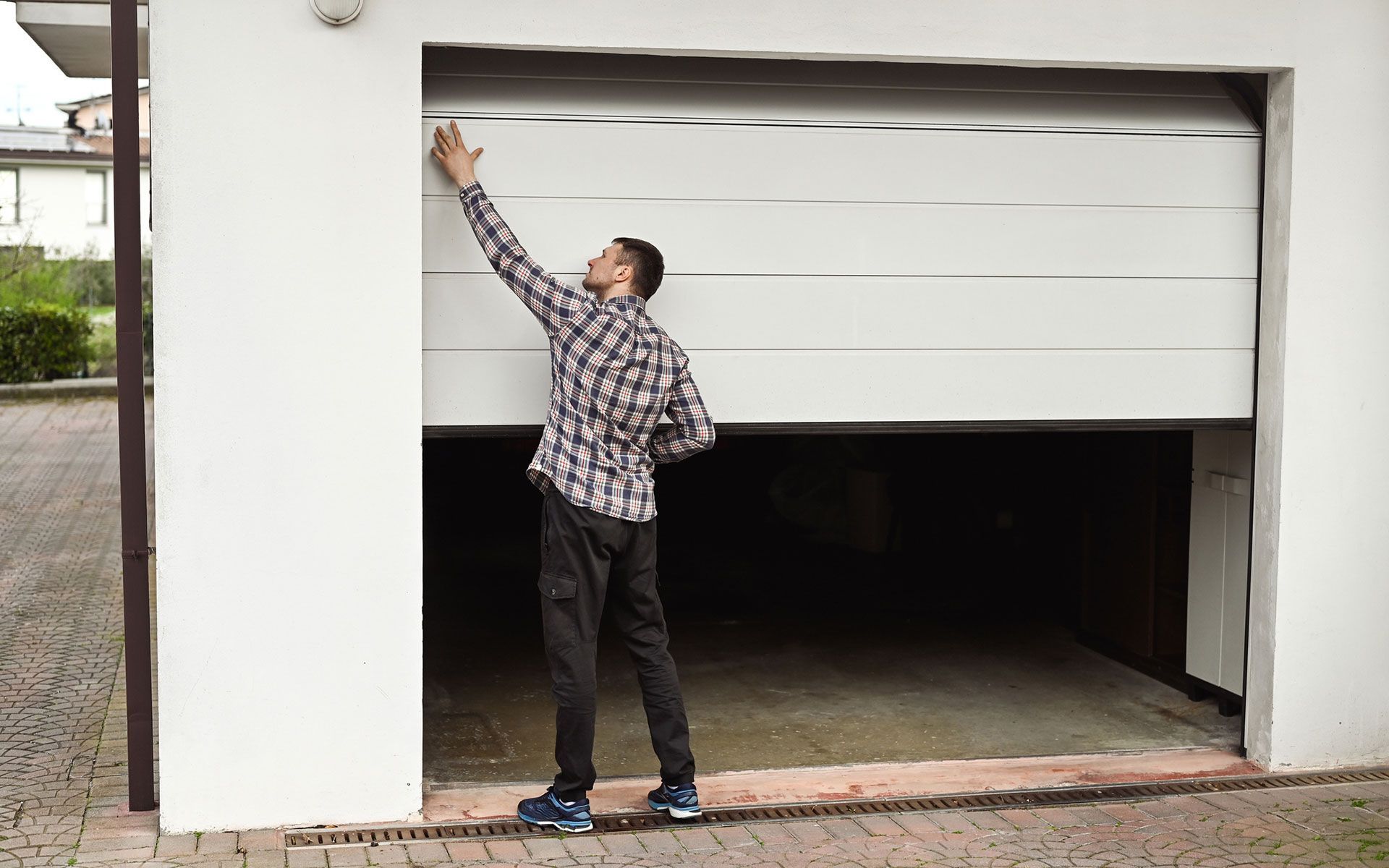 A man in a plaid shirt is opening a garage door.