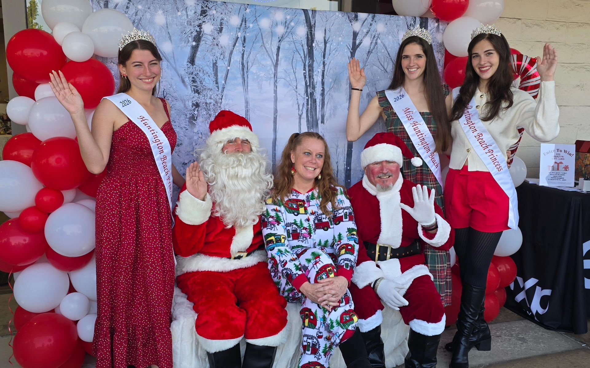 People with Santa and crowns pose in front of a winter-themed backdrop with balloons.