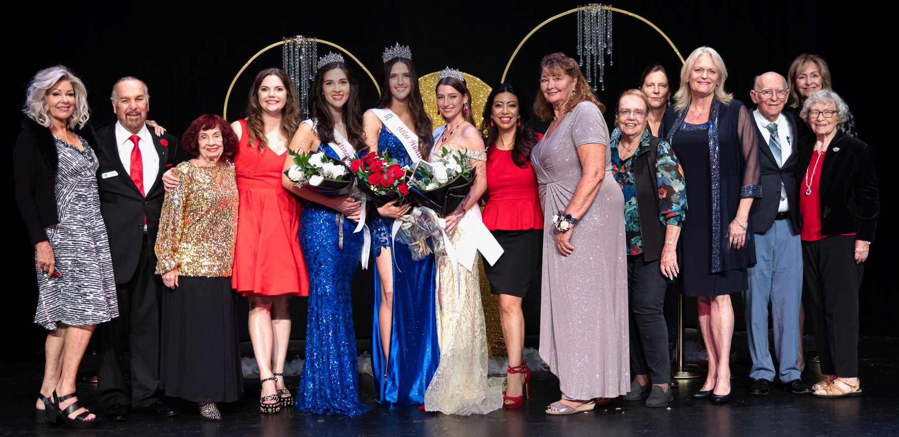 A group of people on a stage with winners holding bouquets, black background.