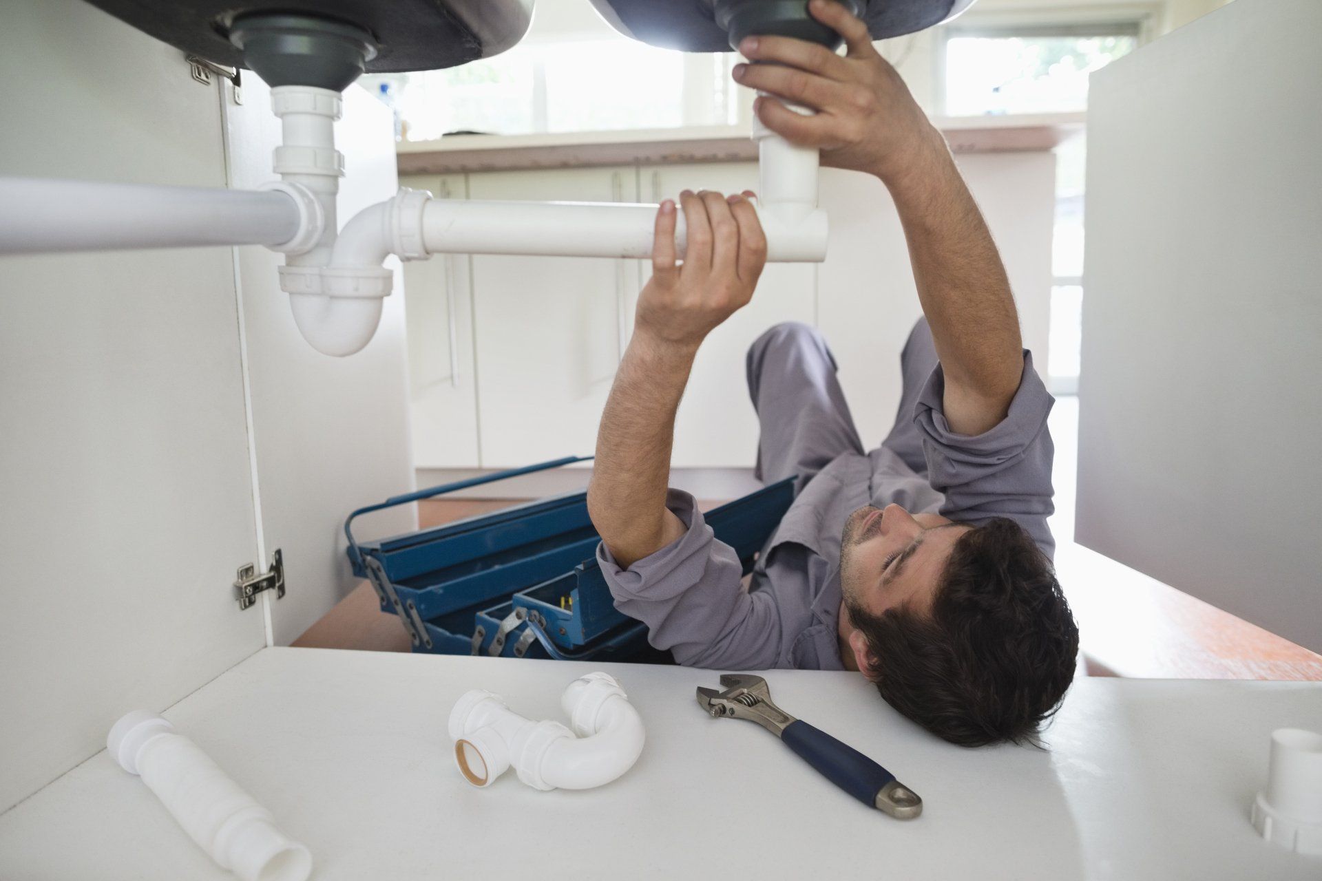 Man Plumber Repairing Pipe Under Sink — Somers Point, NJ — McBride & Company Plumbing, Heating, Air Conditioning