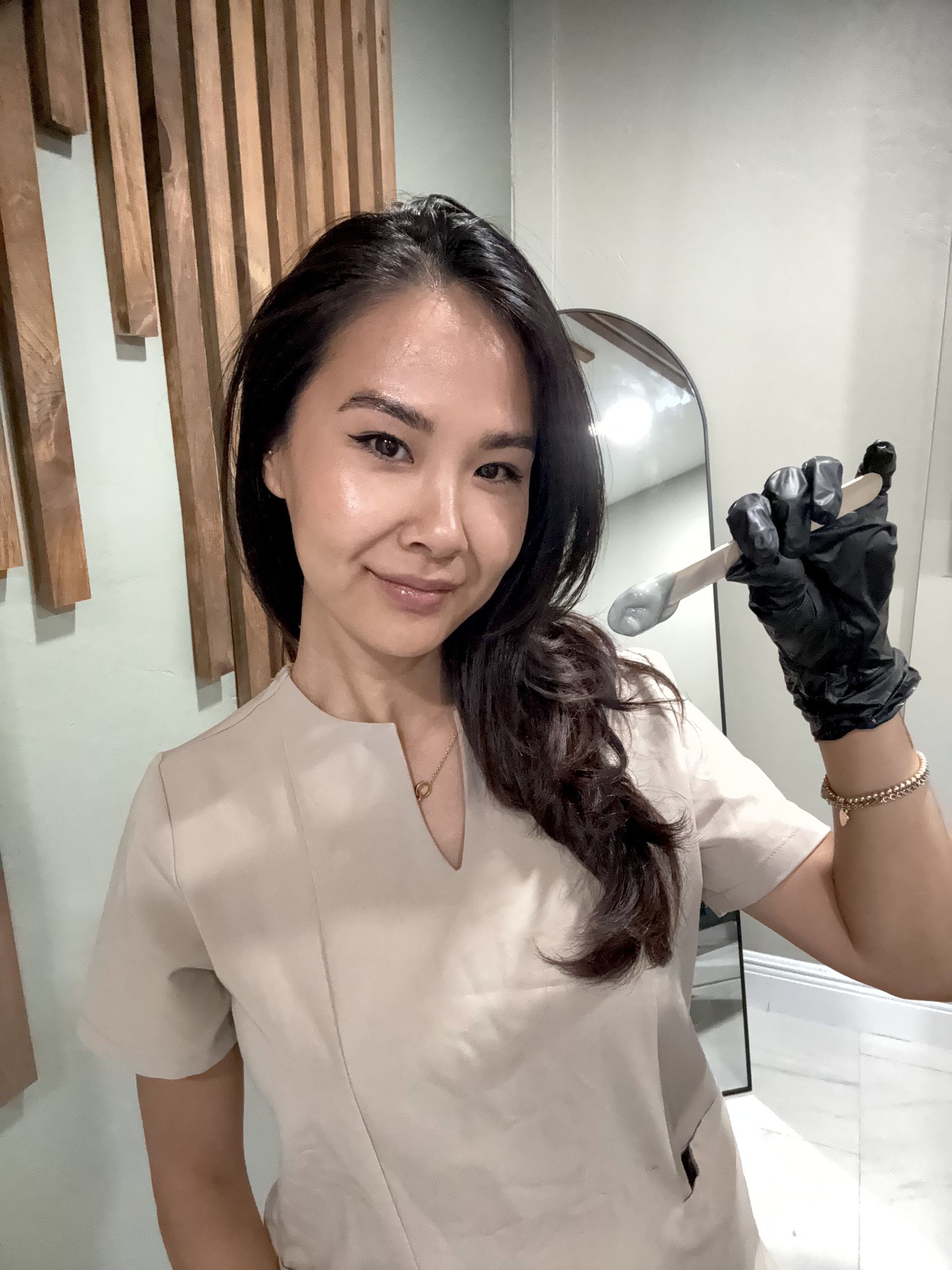 Woman in tan uniform holding a tool, wearing black gloves. Smiling in a professional setting.