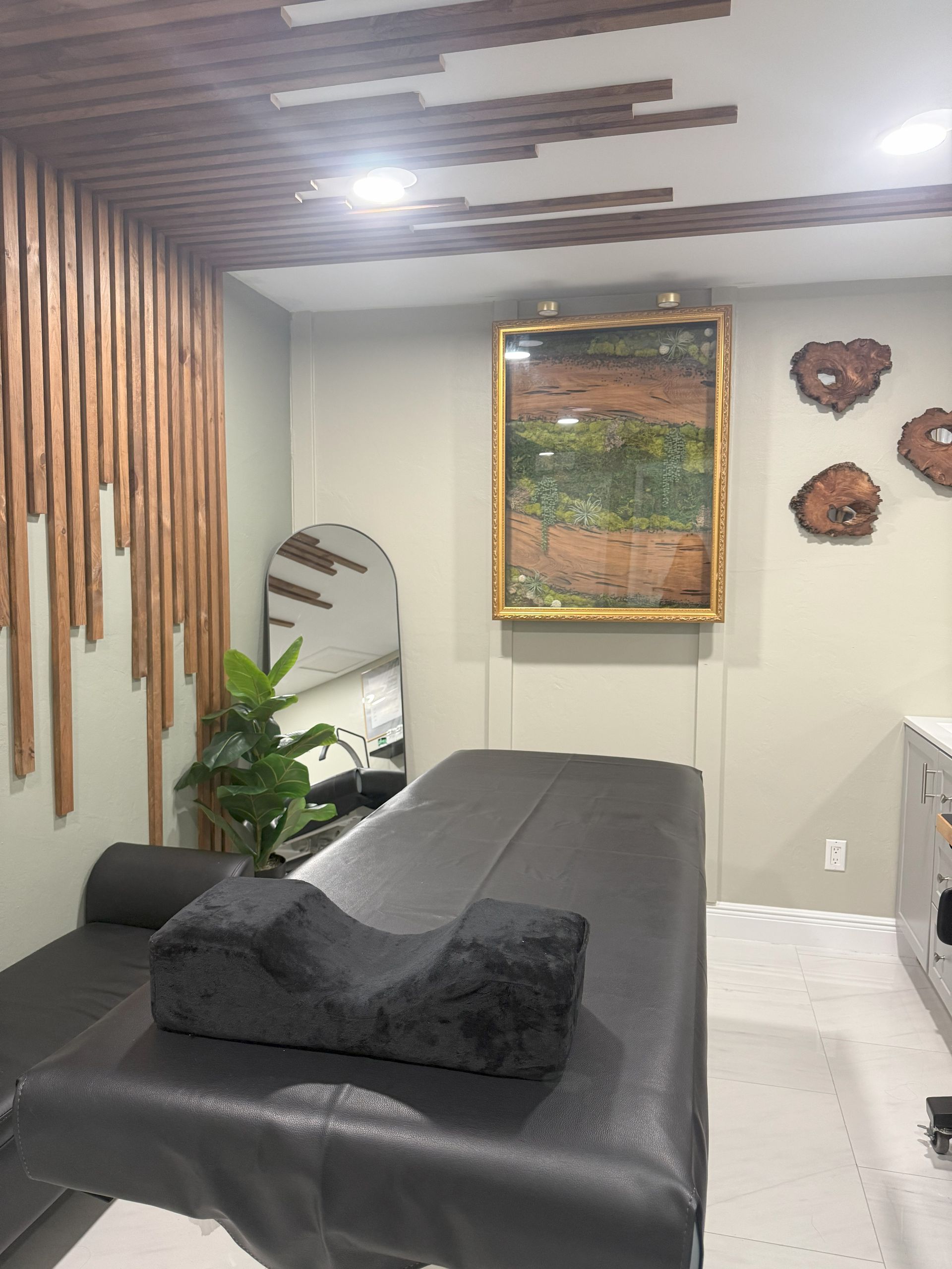 Spa room with massage table, art, wooden accents, and a mirror.