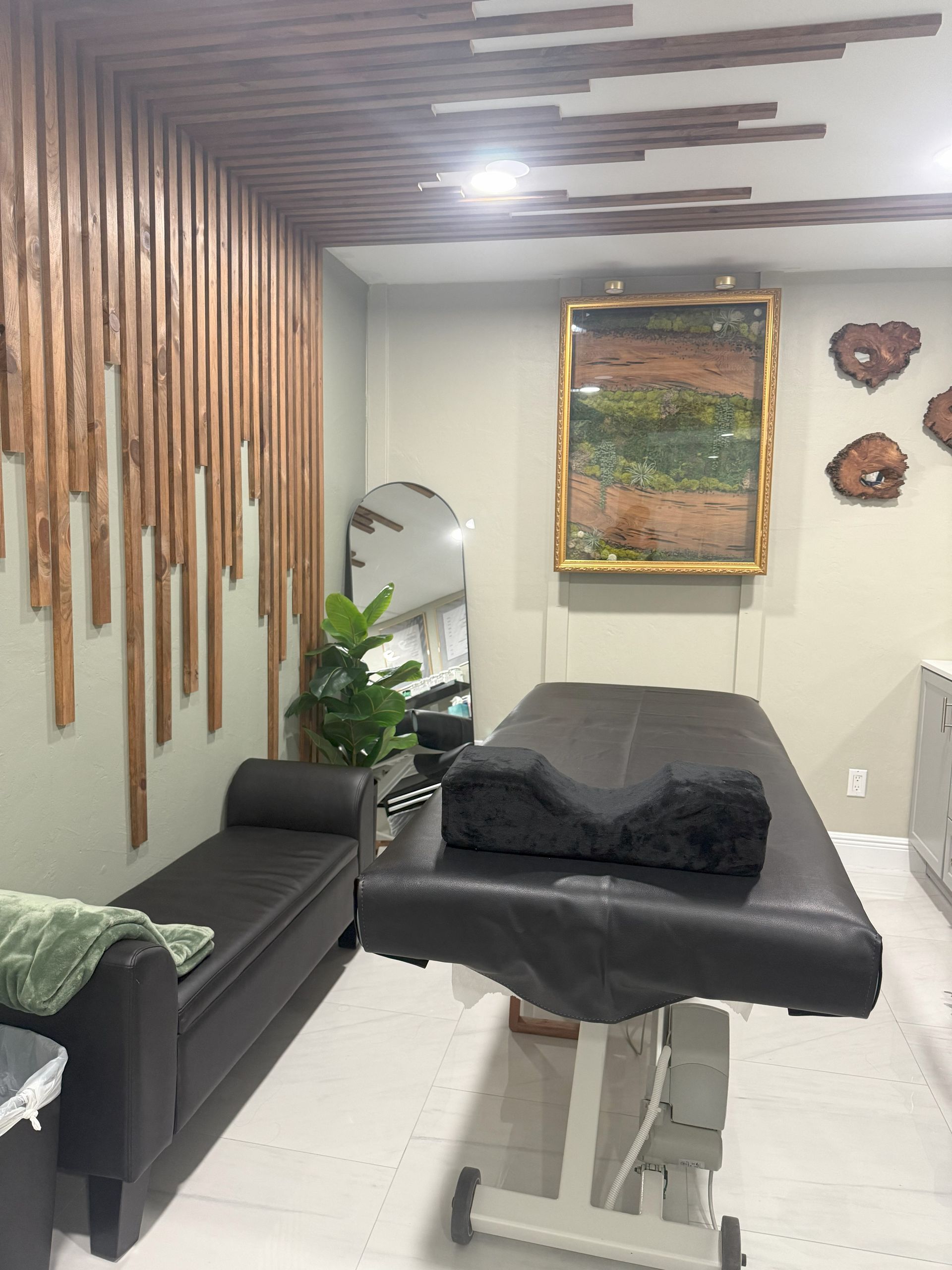 A massage therapy room with a black massage table, bench, and art on the wall.