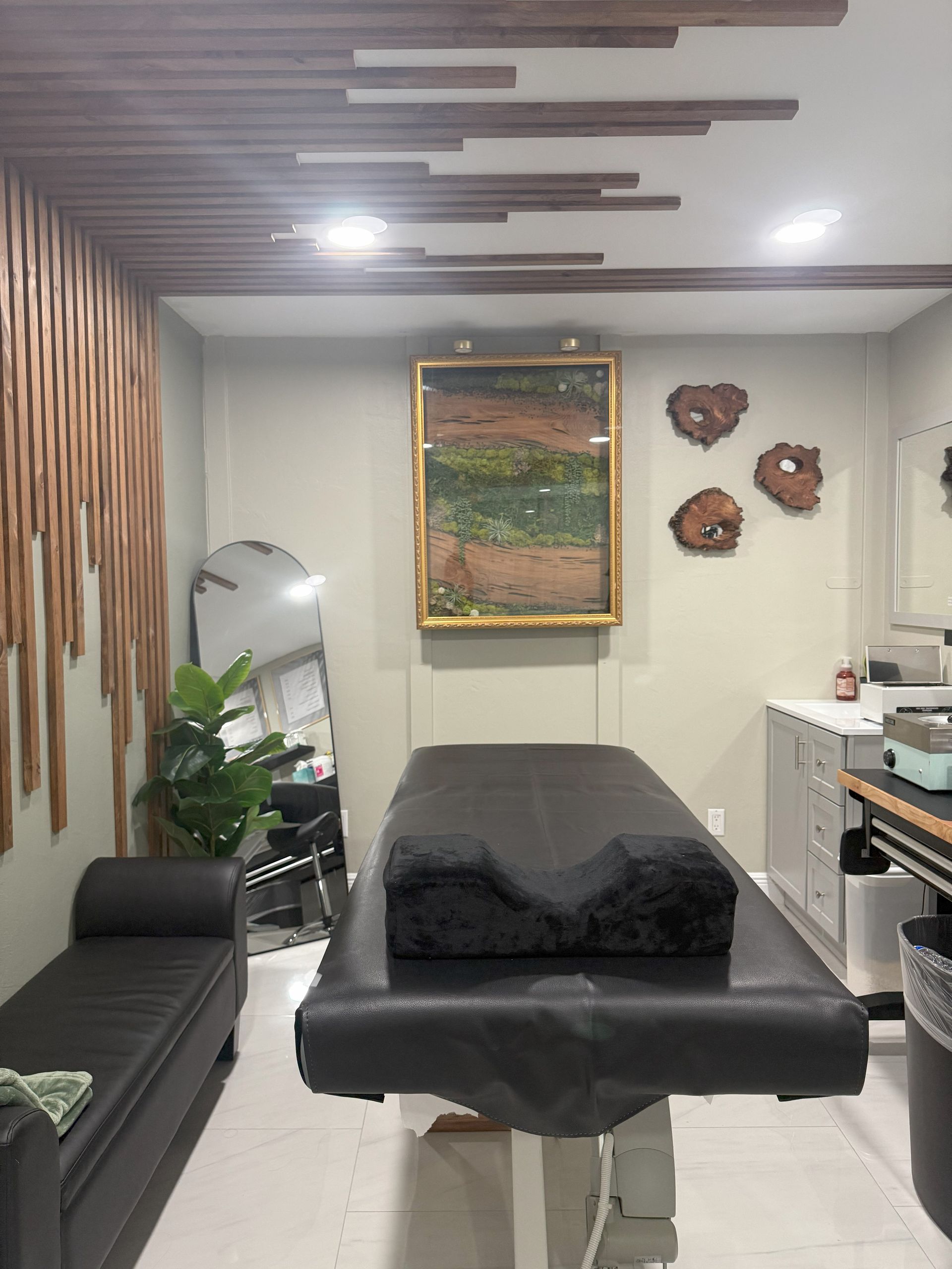 Person wearing black gloves stirs purple wax in a white wax warmer with wooden handle.