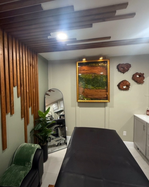 A modern spa room with wooden accents, a treatment table, and artwork on the wall.