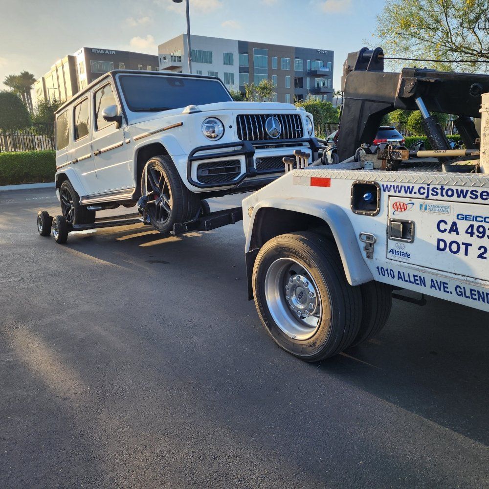 White Mercedes-Benz G-Class SUV being towed by a white tow truck on an asphalt surface.