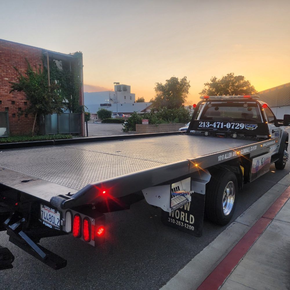 Tow truck with flatbed, parked on a street at sunset.