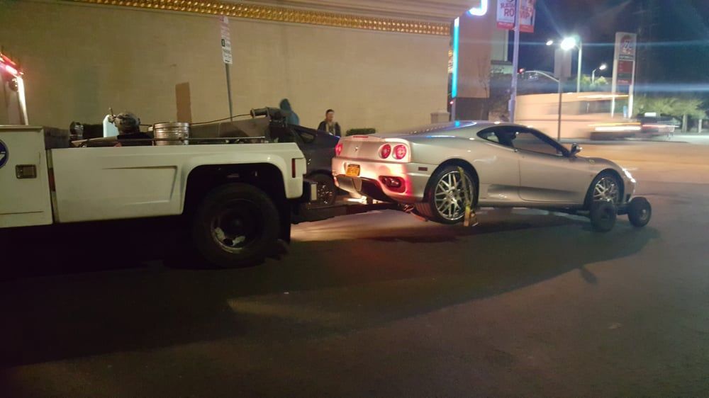 Silver sports car being towed by a tow truck at night.