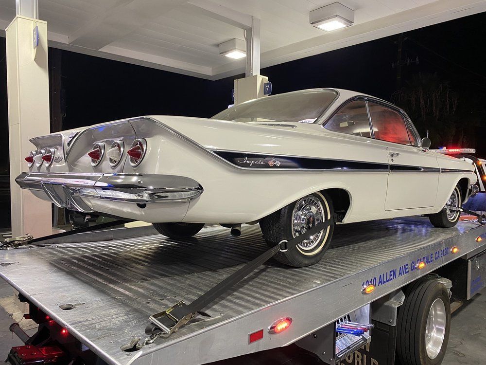 White 1961 Chevrolet Impala on a tow truck at a gas station at night.