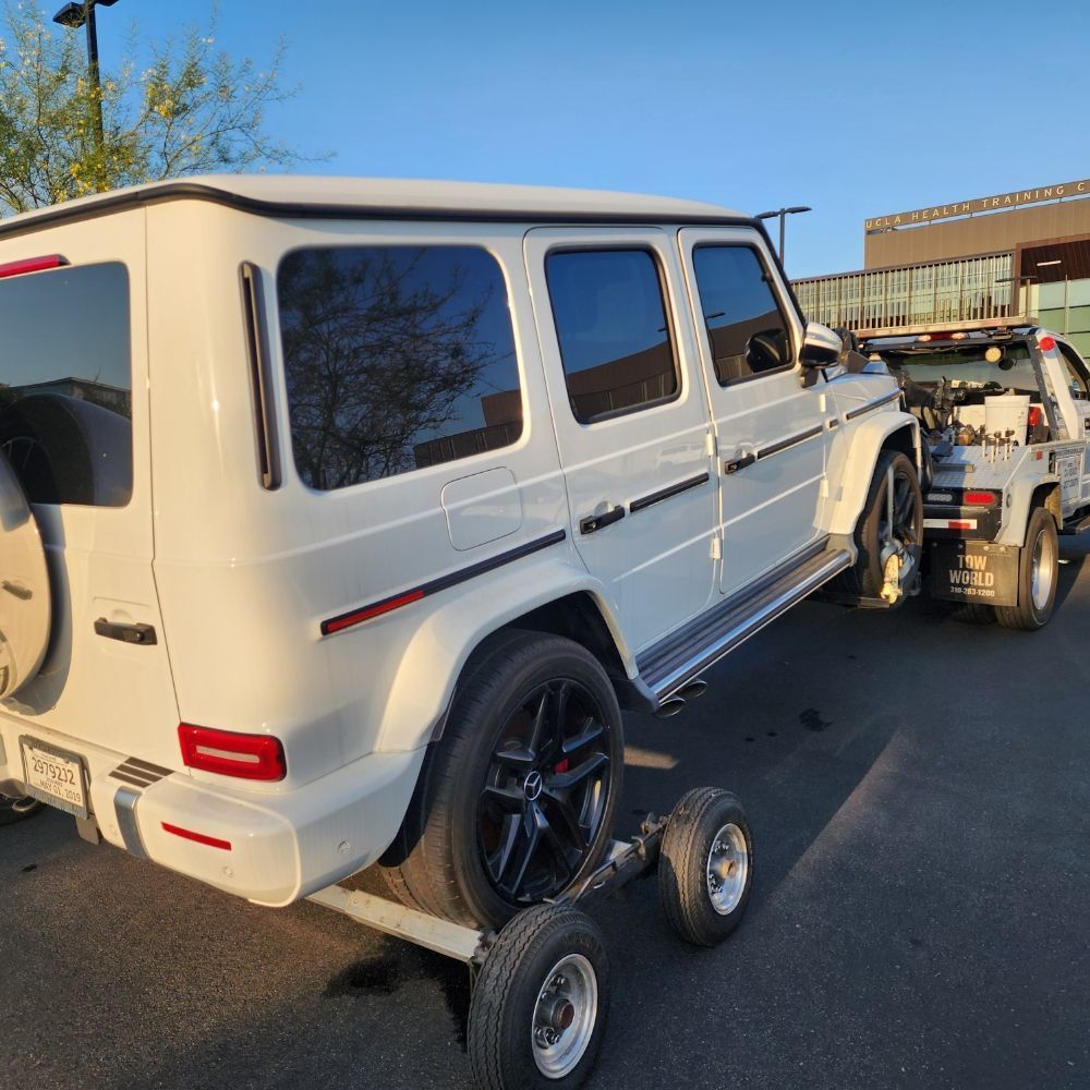 White Mercedes-Benz G-Wagon being towed away on a flatbed trailer.