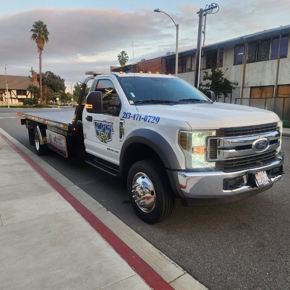 White tow truck parked on the side of a road, displaying a phone number.
