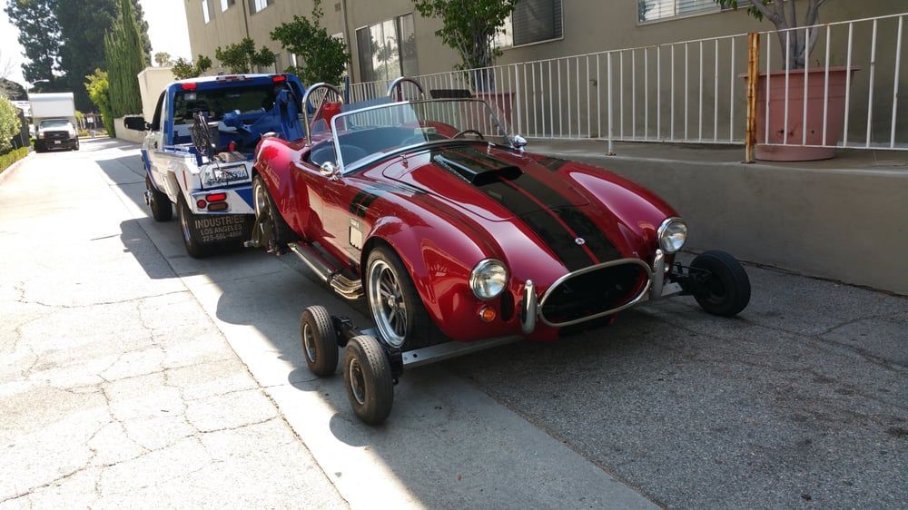 Red Cobra sports car being towed on a flatbed tow truck.