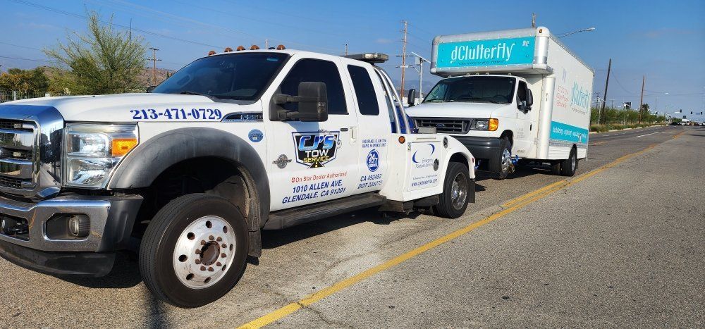 Tow truck towing a white box truck on a sunny road.