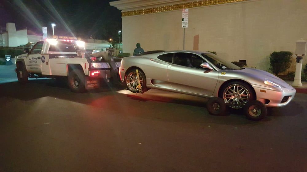 A silver Ferrari being towed by a tow truck at night.