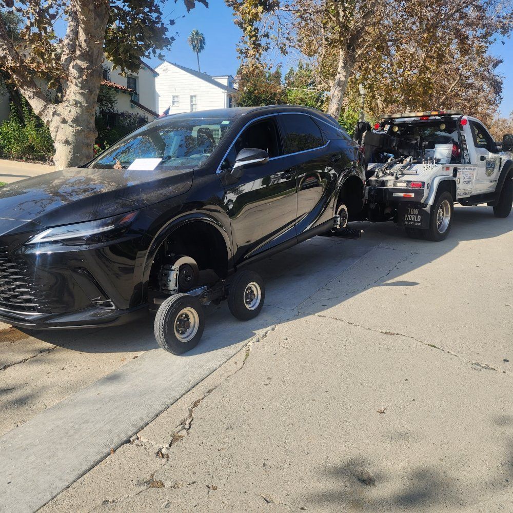 Black car being towed by a tow truck on a street. Car has no front tires.