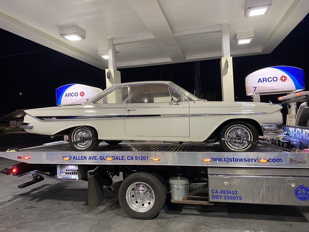 White classic car on a tow truck at a gas station at night.