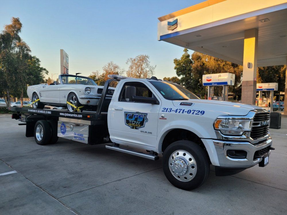 White tow truck carrying a white convertible at a gas station.