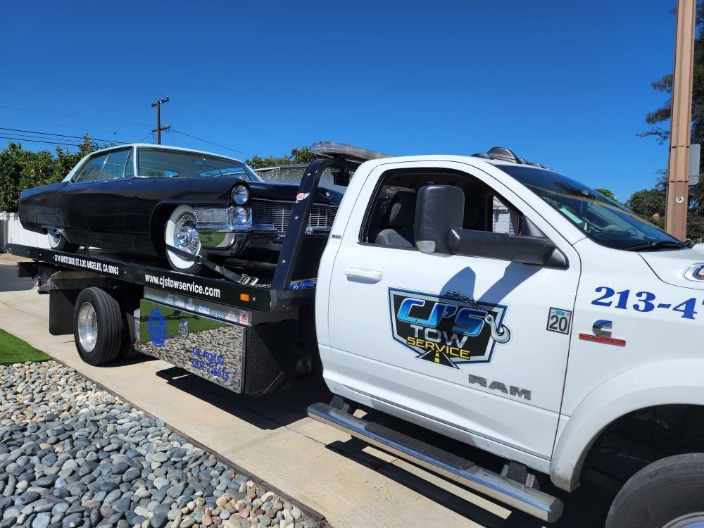 Black classic car being towed on a white tow truck on a sunny day.