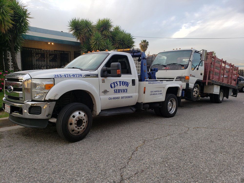 White tow truck towing a white truck on a residential street. The tow truck has 