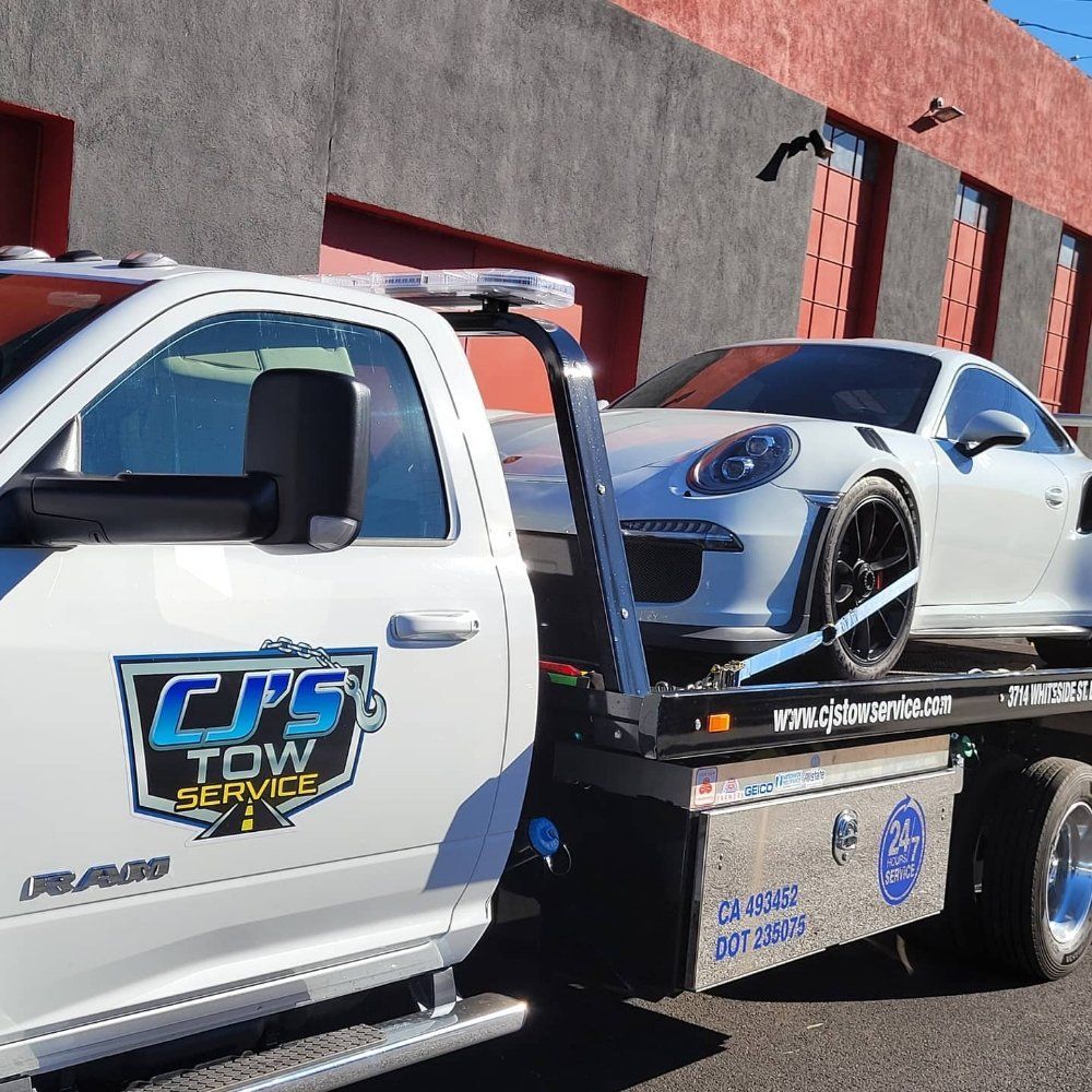 White tow truck towing a white Porsche sports car. The tow truck has 