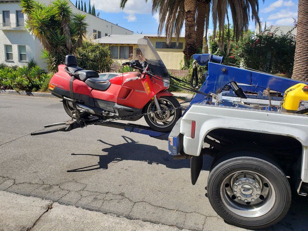 A red motorcycle being towed by a white tow truck on a city street.