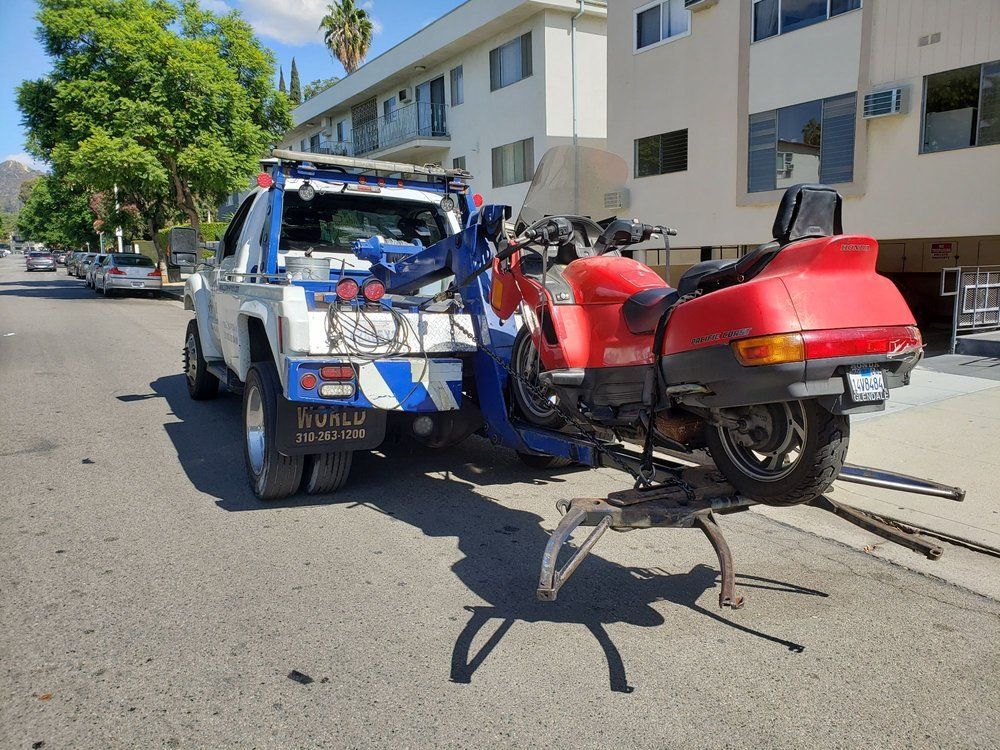 Tow truck towing a red motorcycle on a city street.
