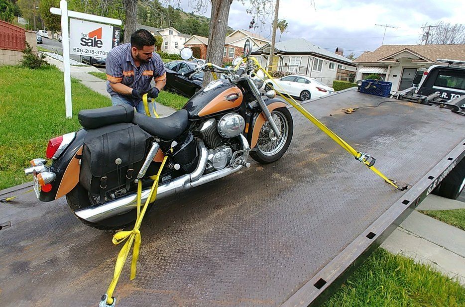 A tow truck operator secures a motorcycle with yellow straps on a ramp.