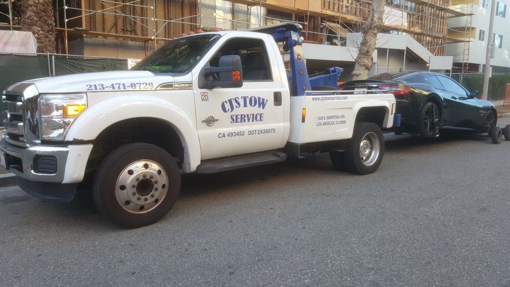 White tow truck towing a black car on a city street.