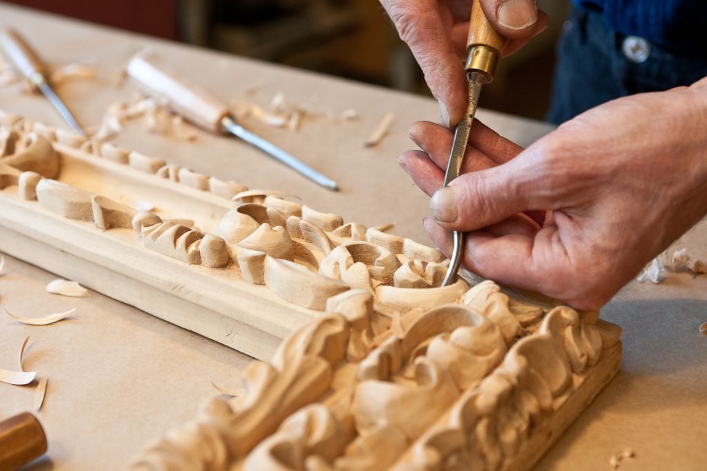 image of two hands with a carving tool working on the corner of an ornate wooden frame