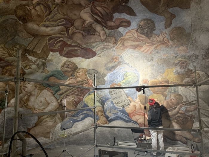A woman retouching a large mural with biblical subject matter