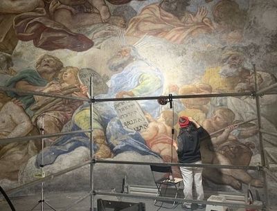 A woman retouching a large mural with biblical subject matter