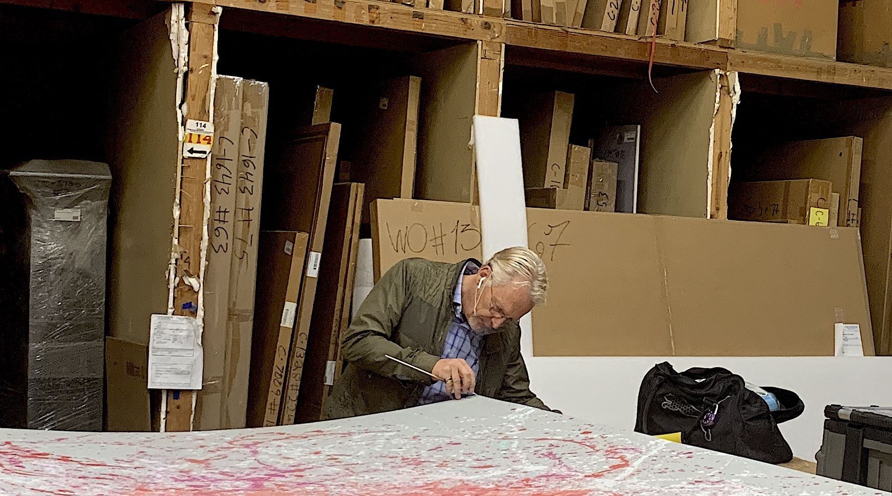 an older white man peeks under the corner of a large abstract artwork 