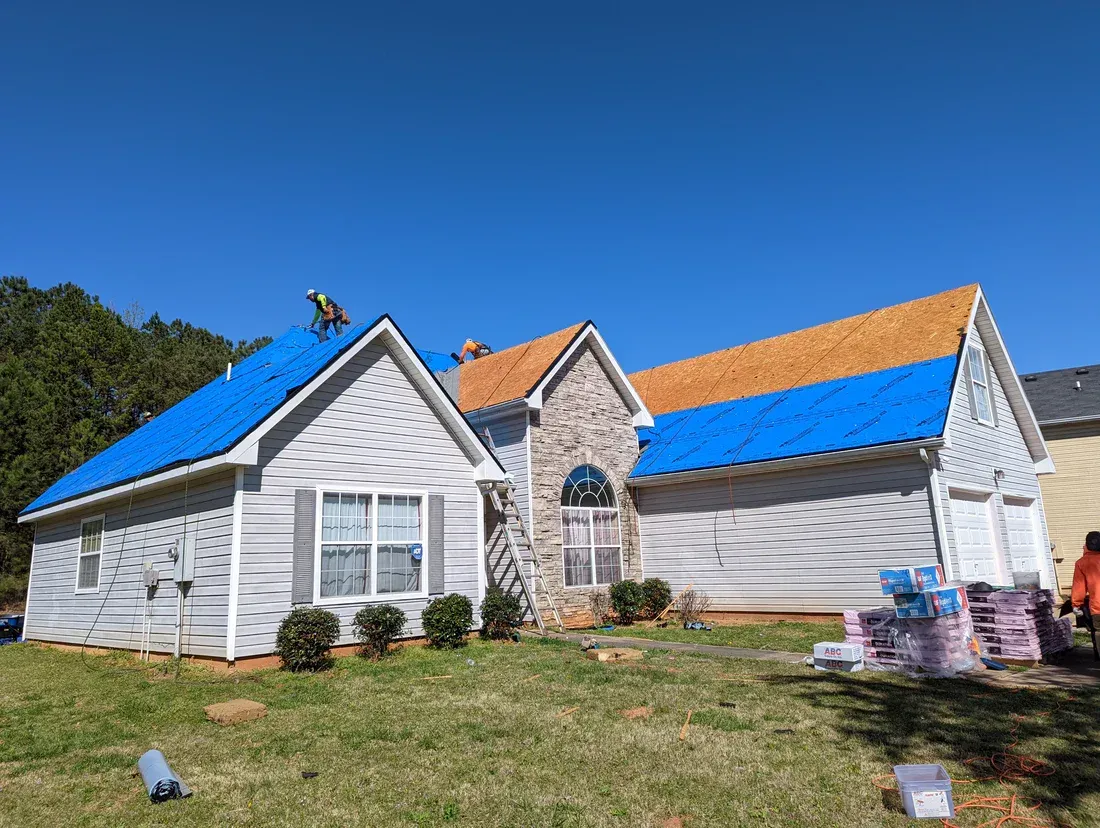 House with roofing work in progress. Blue tarp covers one section, other sections have exposed wood.