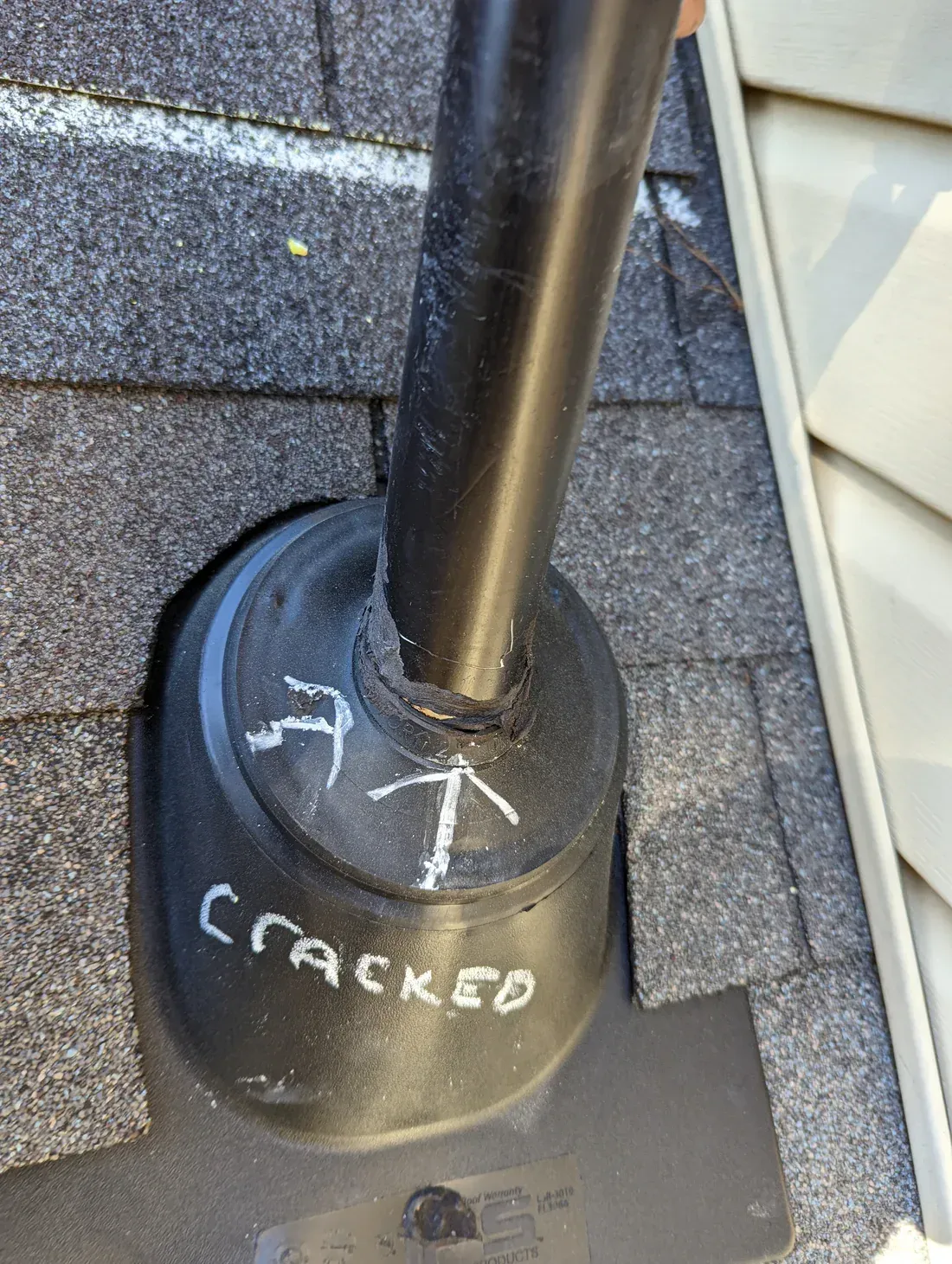 Black plumbing vent pipe protruding from a cracked rubber roof flashing on a shingle roof.