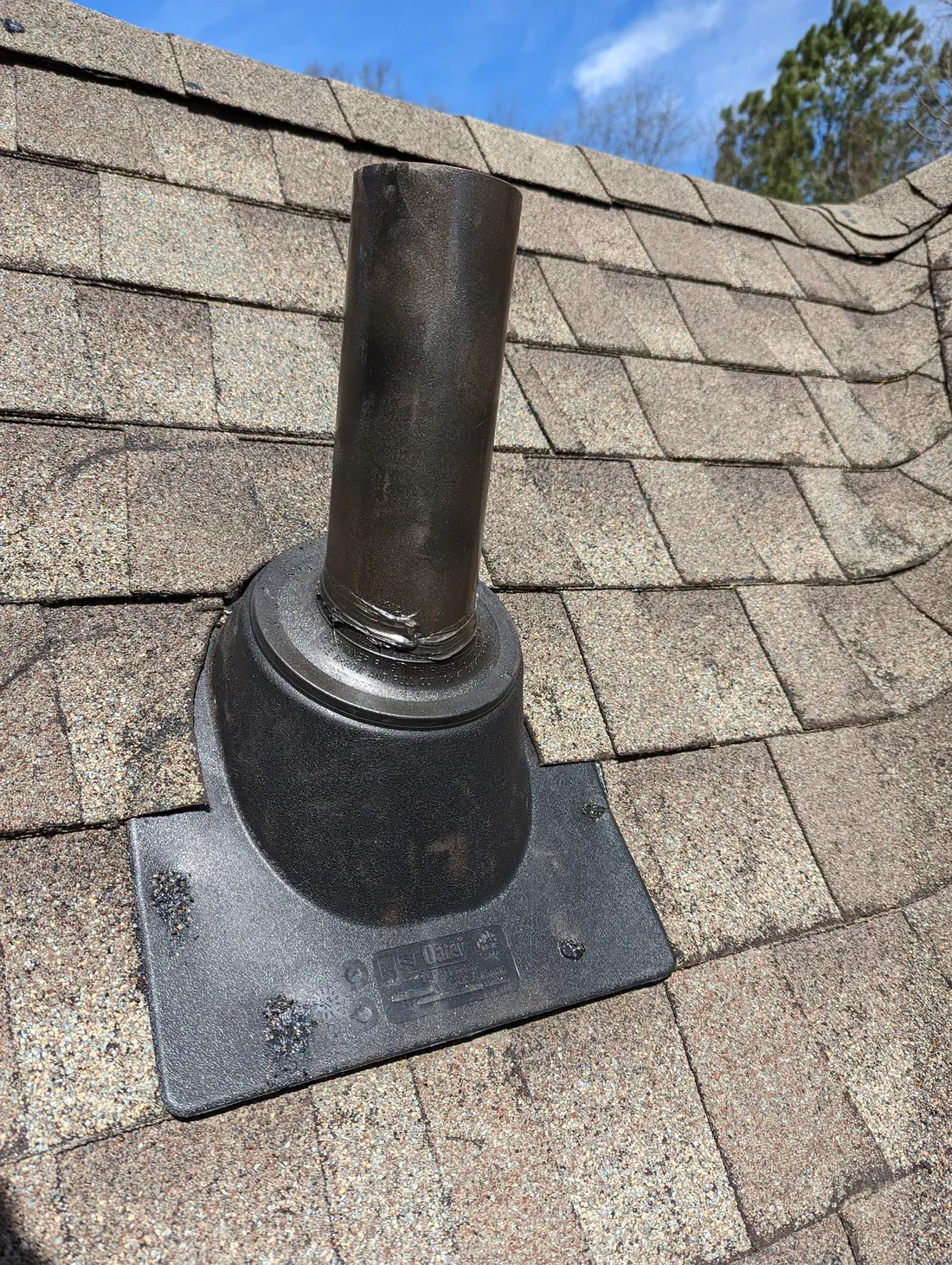 Black vent pipe protruding from a roof, sealed with a rubber boot.