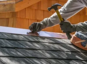 Person hammering metal flashing on a roof, wearing gloves.