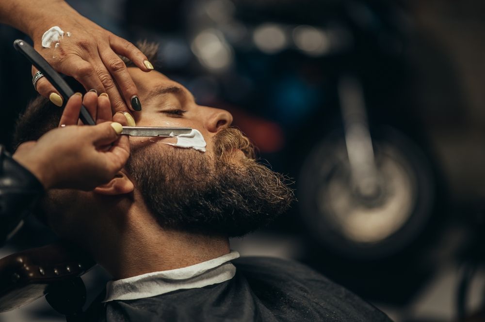 A man is getting his beard shaved by a barber in a barber shop.