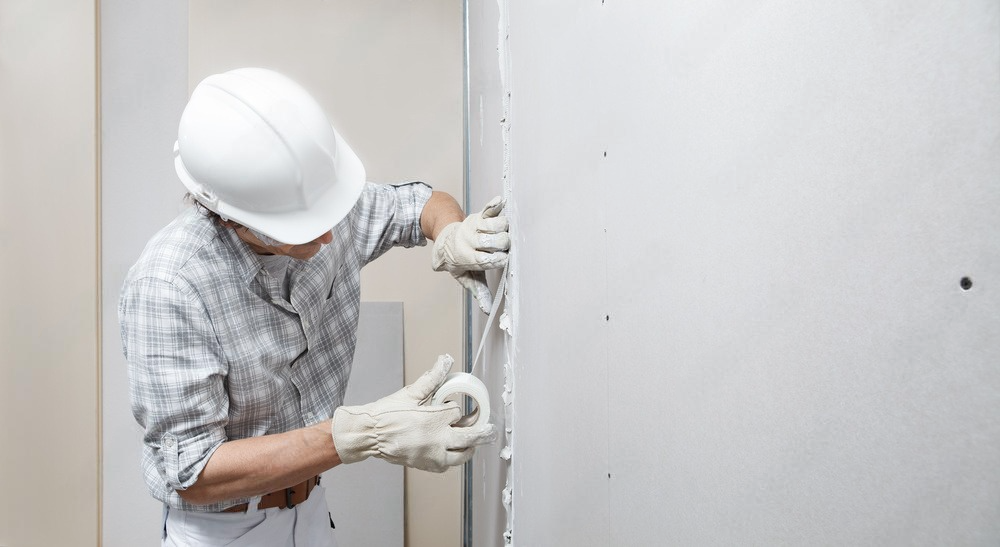 a man wearing a hard hat and gloves is plastering a wall .