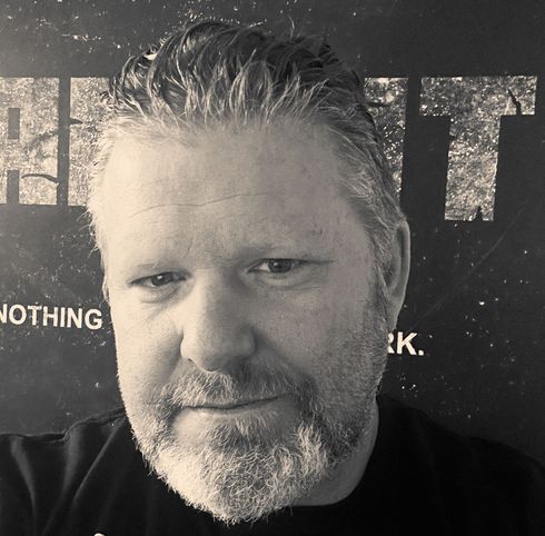 A man with a beard is standing in front of a sign that says nothing