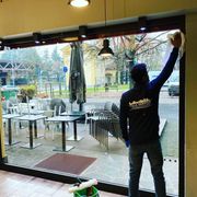Persona che pulisce una grande vetrata di un bar all'aperto.