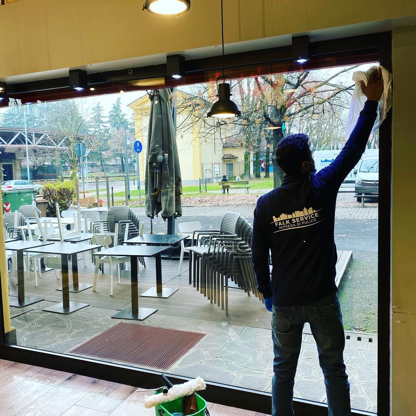 Persona che pulisce una grande vetrata di un bar all'aperto.