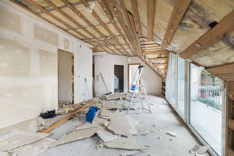 Persona che dipinge un muro con un rullo, coprendo la vernice blu con quella bianca.